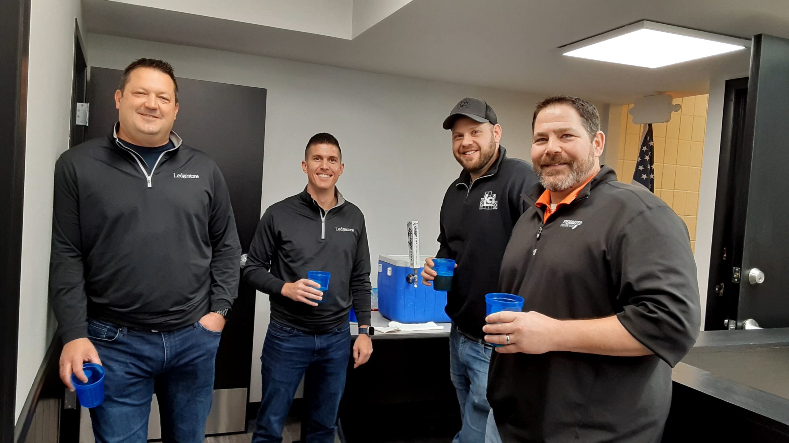 Four men standing in a room holding blue cups.